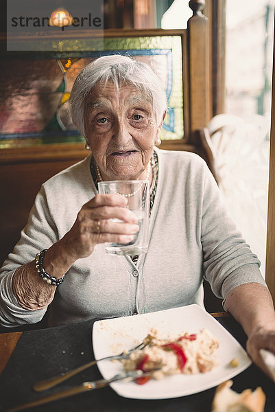 Porträt einer lächelnden Seniorin  die in einem Restaurant Wasser trinkt.