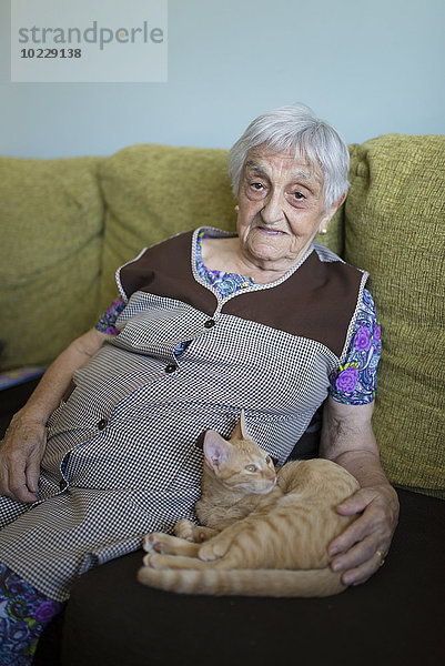 Porträt einer älteren Frau auf der Couch mit getigertem Kätzchen