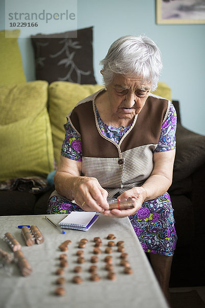 Seniorin sitzt zu Hause auf der Couch und zählt Euro-Cent-Münzen.