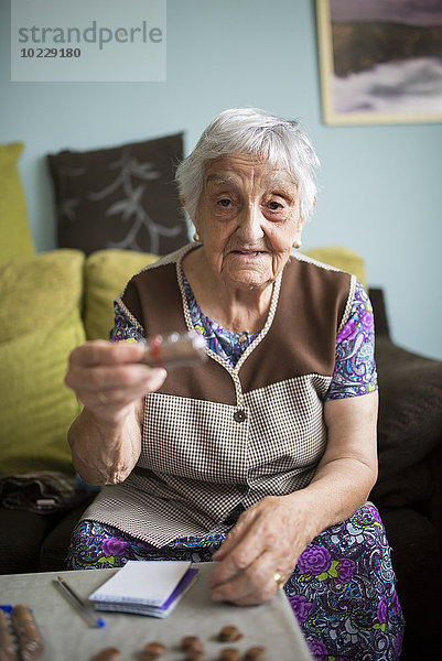 Porträt einer älteren Frau  die zu Hause auf der Couch sitzt und ein Paket mit Münzen zeigt.