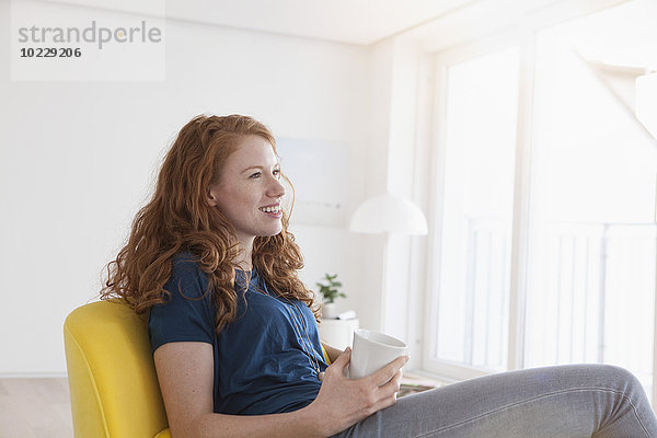Fröhliche junge Frau mit einer Tasse Kaffee in ihrem Wohnzimmer