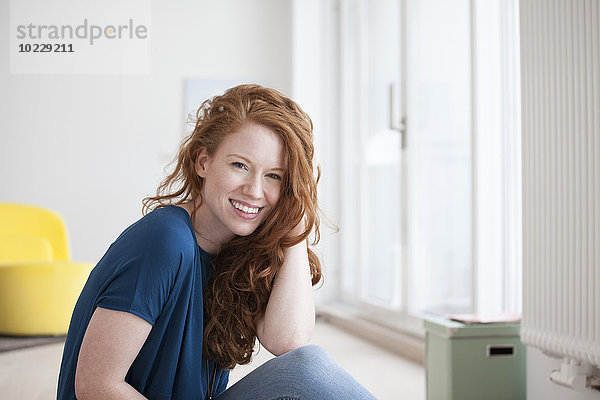 Porträt einer glücklichen jungen Frau  die auf dem Boden ihres Wohnzimmers sitzt.