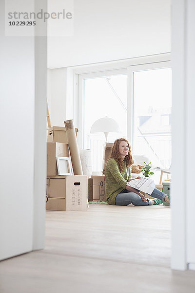 Junge Frau in neuer Wohnung mit Kartons im Grundriss