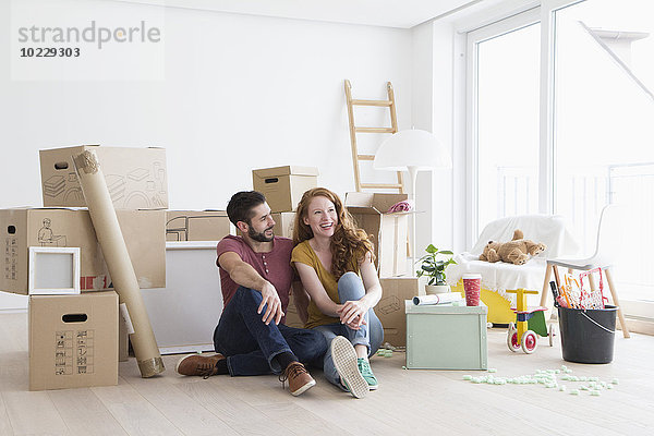 Junges Paar in neuer Wohnung mit Kartons  auf dem Boden sitzend