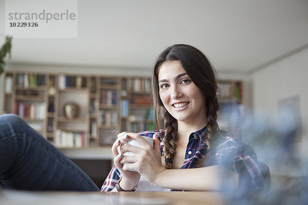 Porträt einer lächelnden jungen Frau mit Kaffeetasse zum Entspannen zu Hause