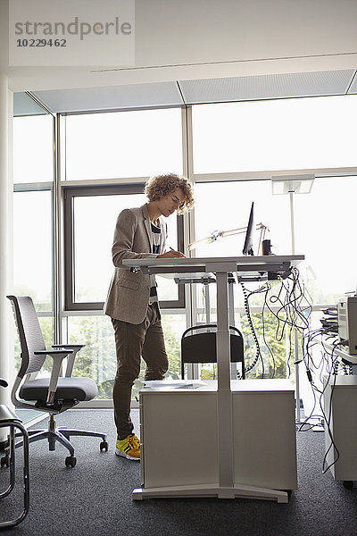 Junger Mann im Büro arbeitet am verstellbaren Schreibtisch