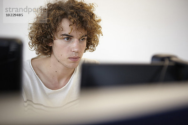 Junger Mann im Büro mit Blick auf den Computerbildschirm