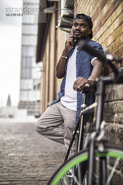 Deutschland  Köln  Portrait eines jungen Mannes mit Fahrradtelefonie mit Smartphone