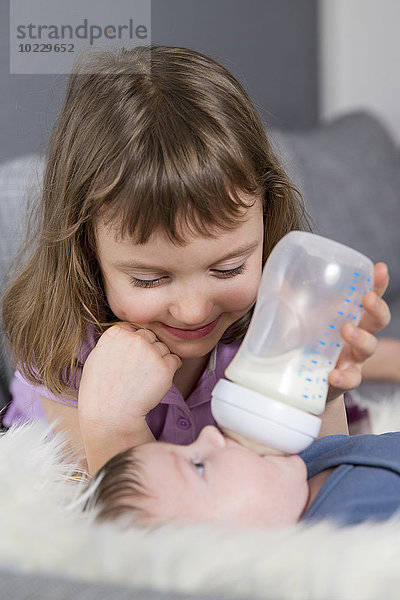 Kleines Mädchen füttert neugeborenen Bruder mit Babyflasche