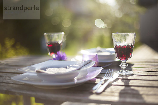 Gedeckter Gartentisch mit zwei Gläsern Rotwein im Gegenlicht