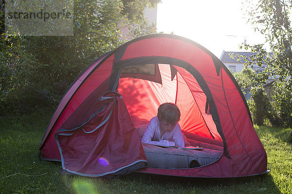 Junge liest in einem roten Zelt in der Abenddämmerung