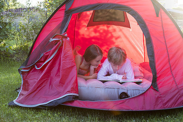 Junge und Mädchen lesen in einem roten Zelt liegend mit einem Buch