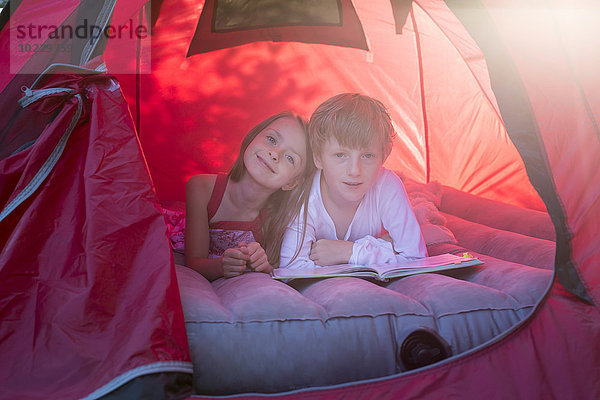 Porträt von Geschwistern im roten Zelt mit Buch
