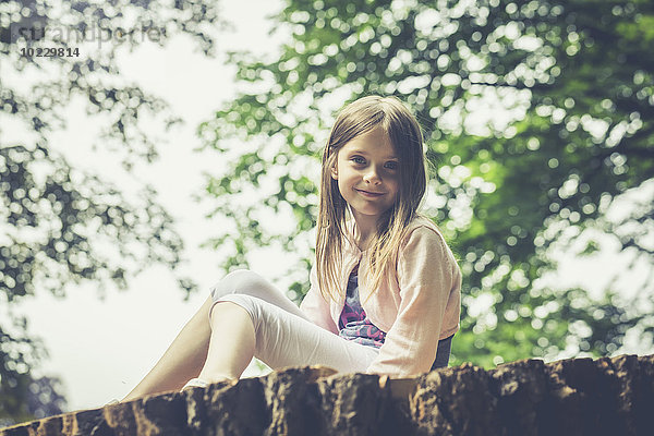 Bildnis eines kleinen Mädchens auf einem großen Baumstamm