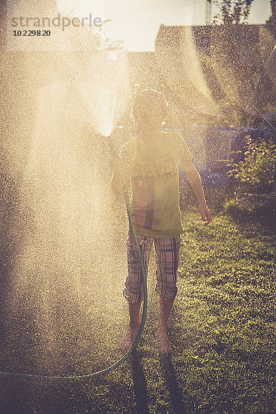 Junge spritzt mit Wasser im Garten