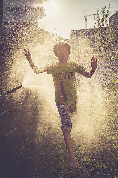 Junge hat Spaß mit Spritzwasser im Garten