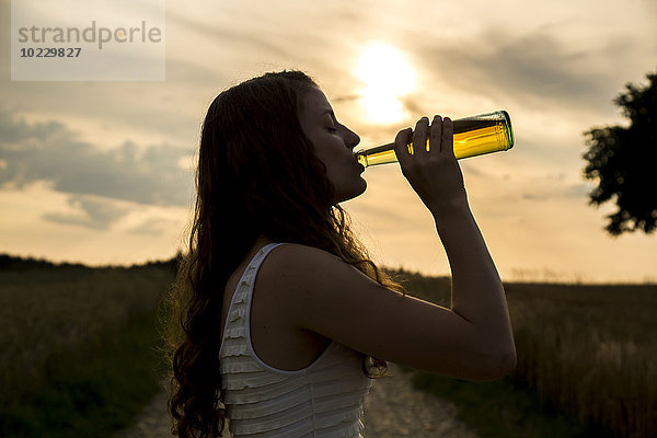 Junge Frau trinkt aus Glasflasche  Abendsonne