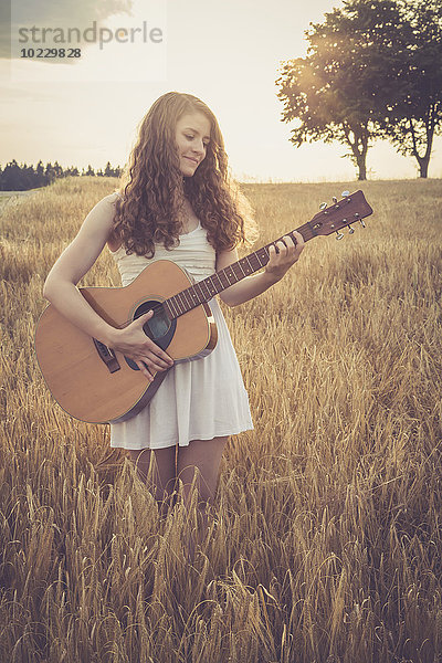 Junge Frau spielt Gitarre im Feld  abends