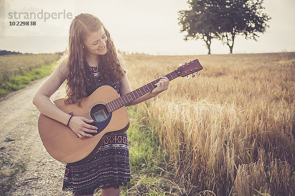Junge Frau spielt Gitarre  Feld am Abend
