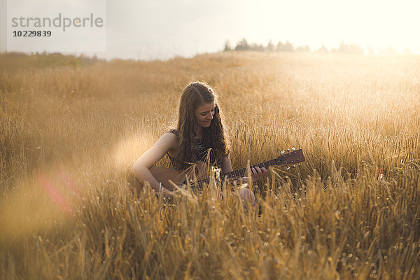 Junge Frau  die abends auf dem Feld Gitarre spielt.