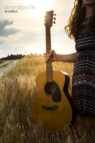 Junge Frau mit Gitarre im Gerstenfeld