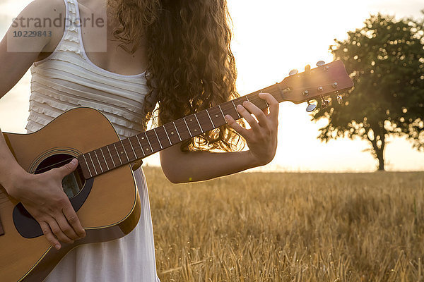 Junge Frau spielt Gitarre  Abendsonne  Gerstenfeld