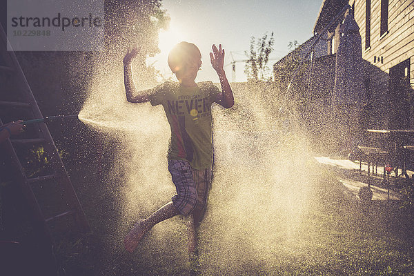 Junge und Mädchen haben Spaß mit spritzendem Wasser im Garten
