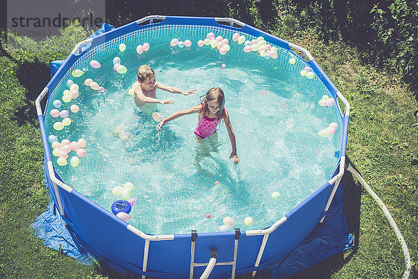 Junge und Mädchen im Schwimmbad umgeben von Luftballons