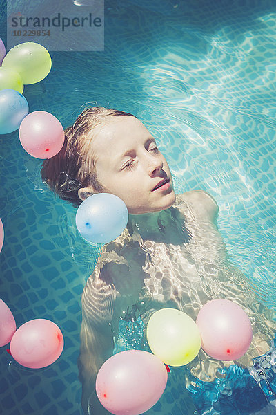 Junge im Schwimmbad  umgeben von Luftballons  die im Wasser schwimmen.