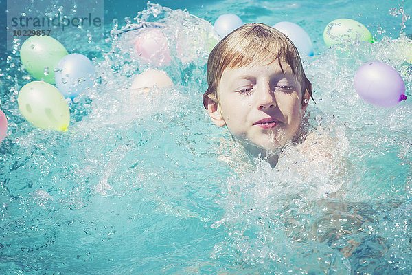 Junge im Schwimmbad umgeben von Luftballons