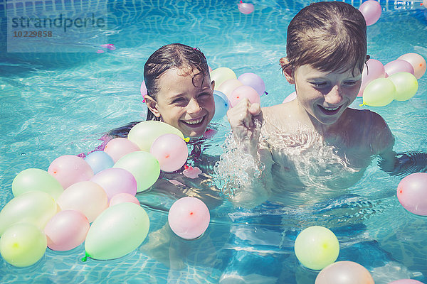 Glückliche Jungen und Mädchen im Schwimmbad  umgeben von Luftballons.