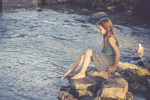 Mädchen sitzt am Wasser und kontrolliert die Temperatur des Wassers.