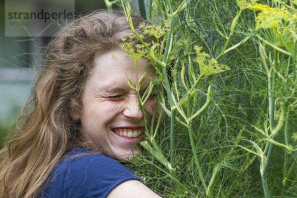 Porträt einer jungen Frau mit geschlossenen Augen  die eine blühende Pflanze umarmt.
