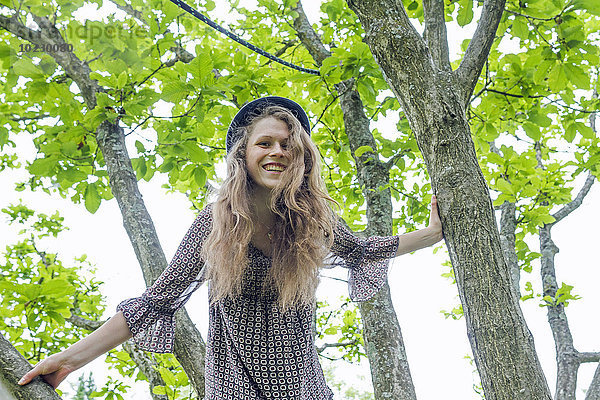 Porträt einer lächelnden jungen Frau  die auf einen Baum klettert.