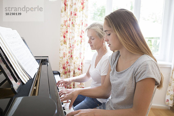 Mutter und Tochter spielen zusammen Klavier