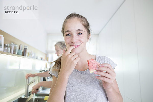 Porträt eines lächelnden Teenagermädchens beim Melonenessen in der Küche