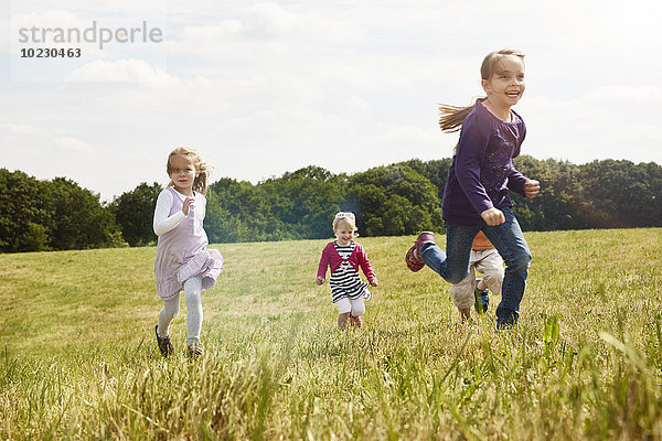 Vier kleine Kinder  die auf einer Wiese rennen.