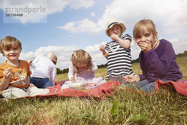 Kinder sitzen auf einer Decke und essen Süßigkeiten.