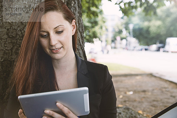 Junge Frau am Baum beim Betrachten des digitalen Tabletts