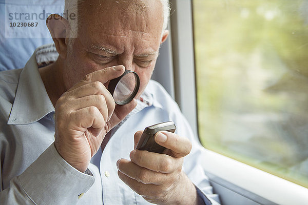 Älterer Mann liest Text auf einem Handy mit Lupe