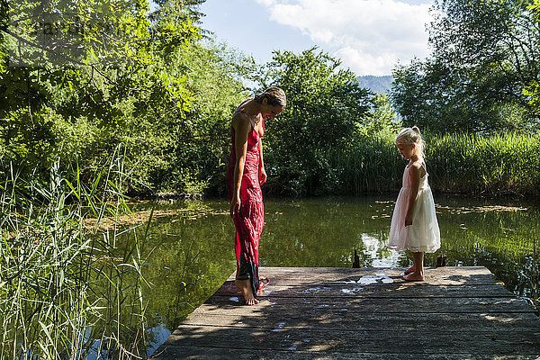 Frau mit nassem Kleid und Tochter am Steg am See