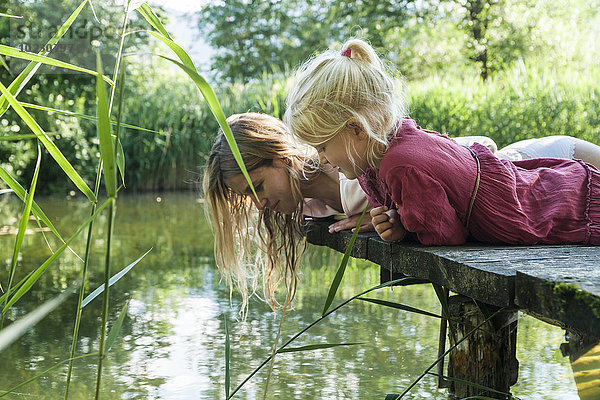 Mutter und Tochter liegen auf einem Steg am See und schauen auf das Wasser.