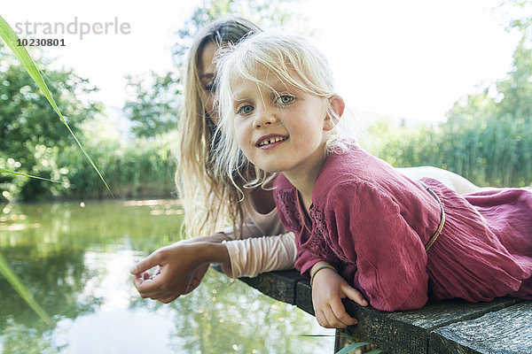 Mutter und lächelnde Tochter liegen auf einem Steg am See.