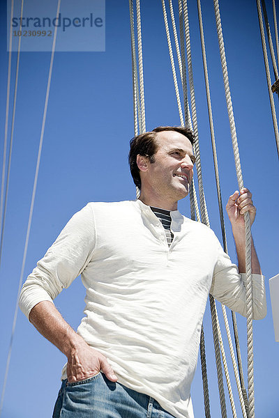Erwachsener Mann auf einem Segelschiff  der ein Seil hält.