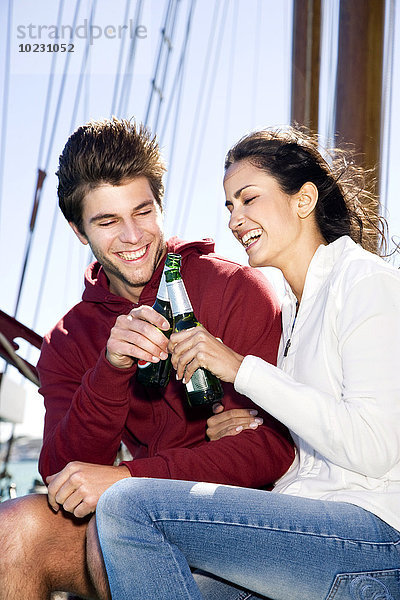 Glücklicher junger Mann und Frau klirrende Bierflaschen auf einem Segelschiff