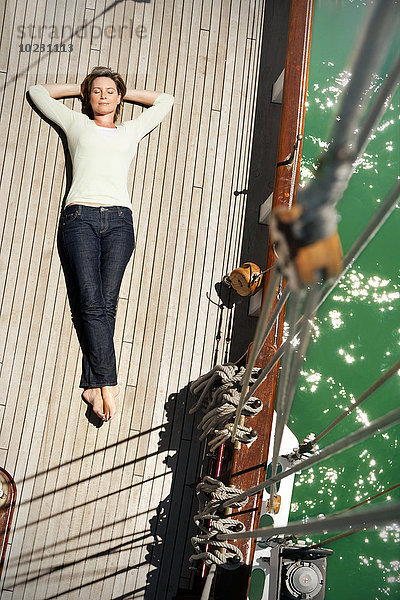 Entspannte reife Frau auf dem Deck eines Segelschiffes liegend