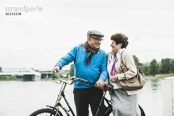 Fröhliches Seniorenpaar am Wasser stehend mit Fahrrad