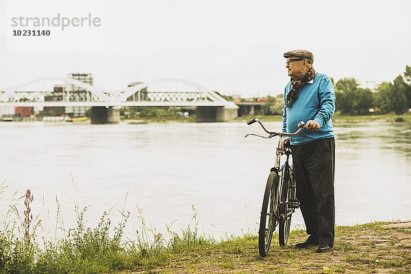 Älterer Mann mit dem Fahrrad am Wasser stehend