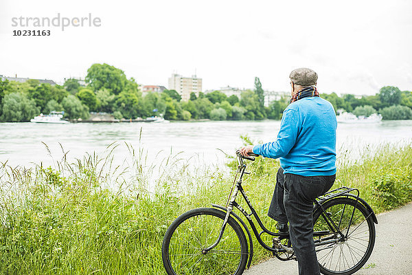 Älterer Mann mit Fahrrad mit Blick auf den Fluss