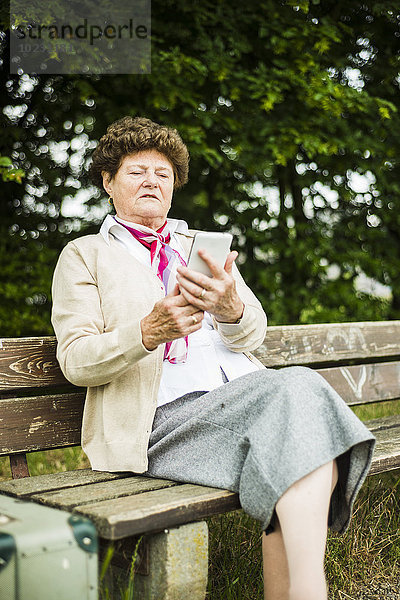 Seniorin auf der Bank sitzend mit Phablet